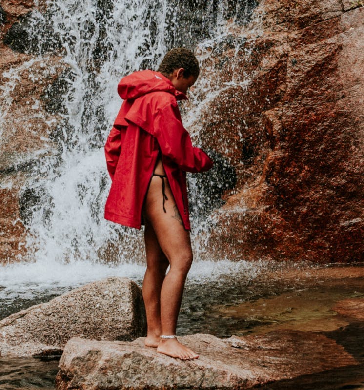 A person in a red jacket stand on a rock in front of a waterfall